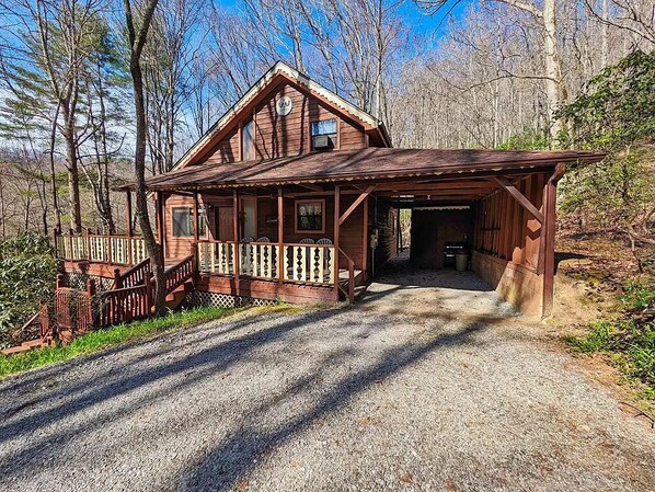 Una baita di legno con veranda e garage, immersa tra gli alberi.