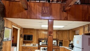 A rustic kitchen with wooden walls, a welcome sign, a no smoking sign, and basic appliances. - My Cabin In The Mountain (Otto)