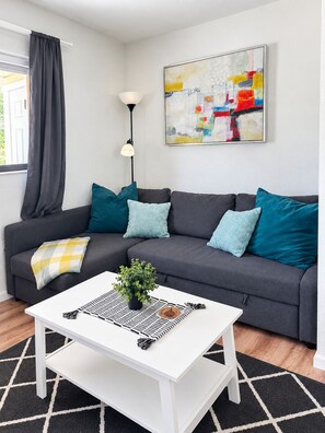 A modern living room with a grey sofa, teal cushions, a white coffee table with a plant, and a colorful abstract painting on the wall. - Sandy Feet Retreat 1A - Minutes to Sanibel - Pool - fast WiFi - free Parking (Fort Myers)