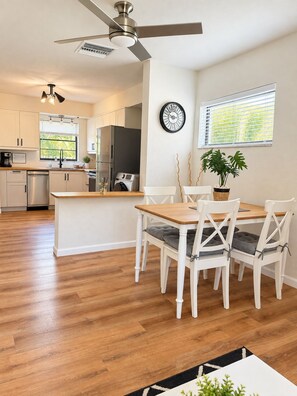 A modern kitchen with white cabinetry, a central island, and a dining area with white chairs and a wooden table.