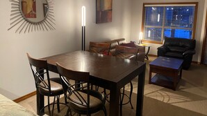 A dining area with a large table, chairs, a sofa, and a window with blinds.