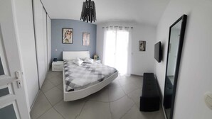 Ein Schlafzimmer mit einem Bett, einem Nachttisch, einem Spiegel und einem Fenster mit Vorhängen.