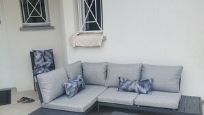 Ein graues Ecksofa mit gestreiften Kissen, ein passendes Ottomanen und zwei Fenster mit weißen Rahmen und Kreuzverstrebungen.