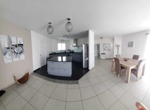 A spacious living area with a central island, a dining table with chairs, and a kitchen in the background. - Very pleasant villa with swimming pool (Ondres)