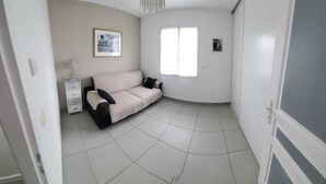Ein Zimmer mit einem beigen Sofa, einem kleinen Nachttisch mit Lampe und einem gerahmten Bild an der Wand.