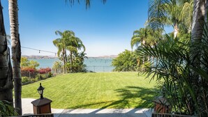 A well-maintained lawn with a pathway leading to a body of water, surrounded by palm trees and a clear sky. - Waterfront Lakeside Mansion Great for Large Families, Retreat, and Events  (Lake Elsinore)