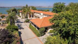 A coastal property with a large house featuring a red-tiled roof, a balcony, and a view of the sea. - Waterfront Lakeside Mansion Great for Large Families, Retreat, and Events  (Lake Elsinore)