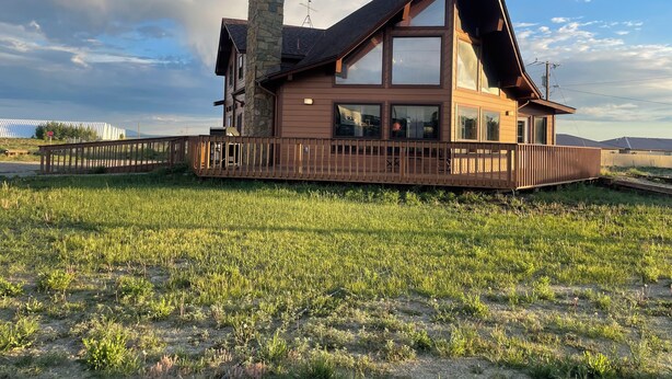 A two-story house with a stone chimney, large windows, and a wooden deck. - Main Street Cabin near Sand Dunes - Fort Garland (Fort Garland)