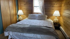 A bedroom with a bed, two bedside lamps, a window with curtains, and wooden walls. - Main Street Cabin near Sand Dunes - Fort Garland (Fort Garland)