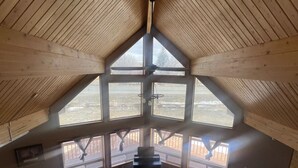 A high-ceilinged room with large windows, a wooden floor, and a central seating area with sofas. - Main Street Cabin near Sand Dunes - Fort Garland (Fort Garland)