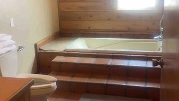 A small, compact bathroom with a wooden floor, a toilet, a sink, and a bathtub.