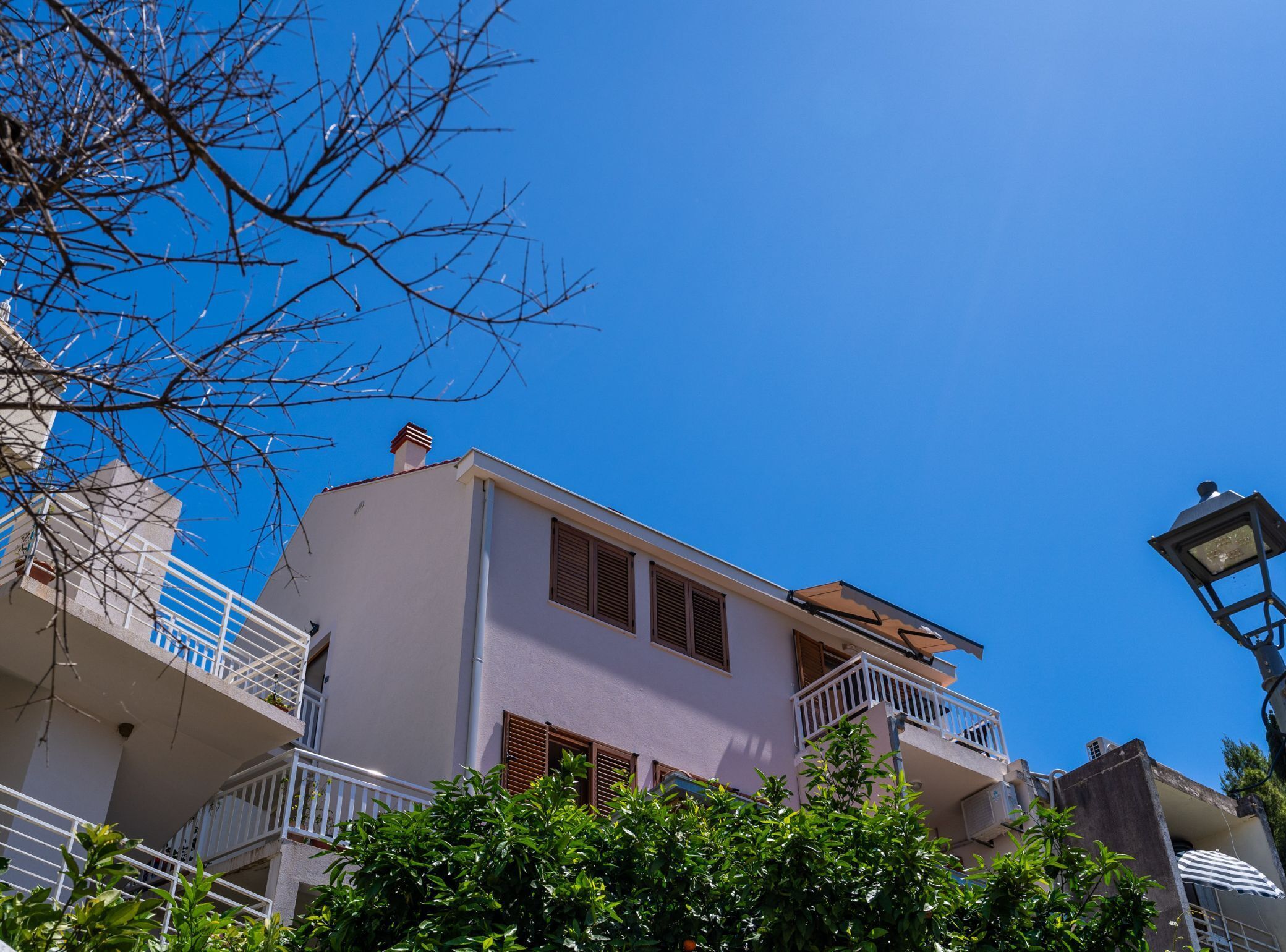 A two-story building with balconies, a clear blue sky, and some greenery in the foreground.