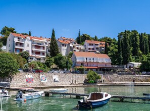 Un pueblo costero con un puerto deportivo, edificios con tejados rojos y un muro de piedra.