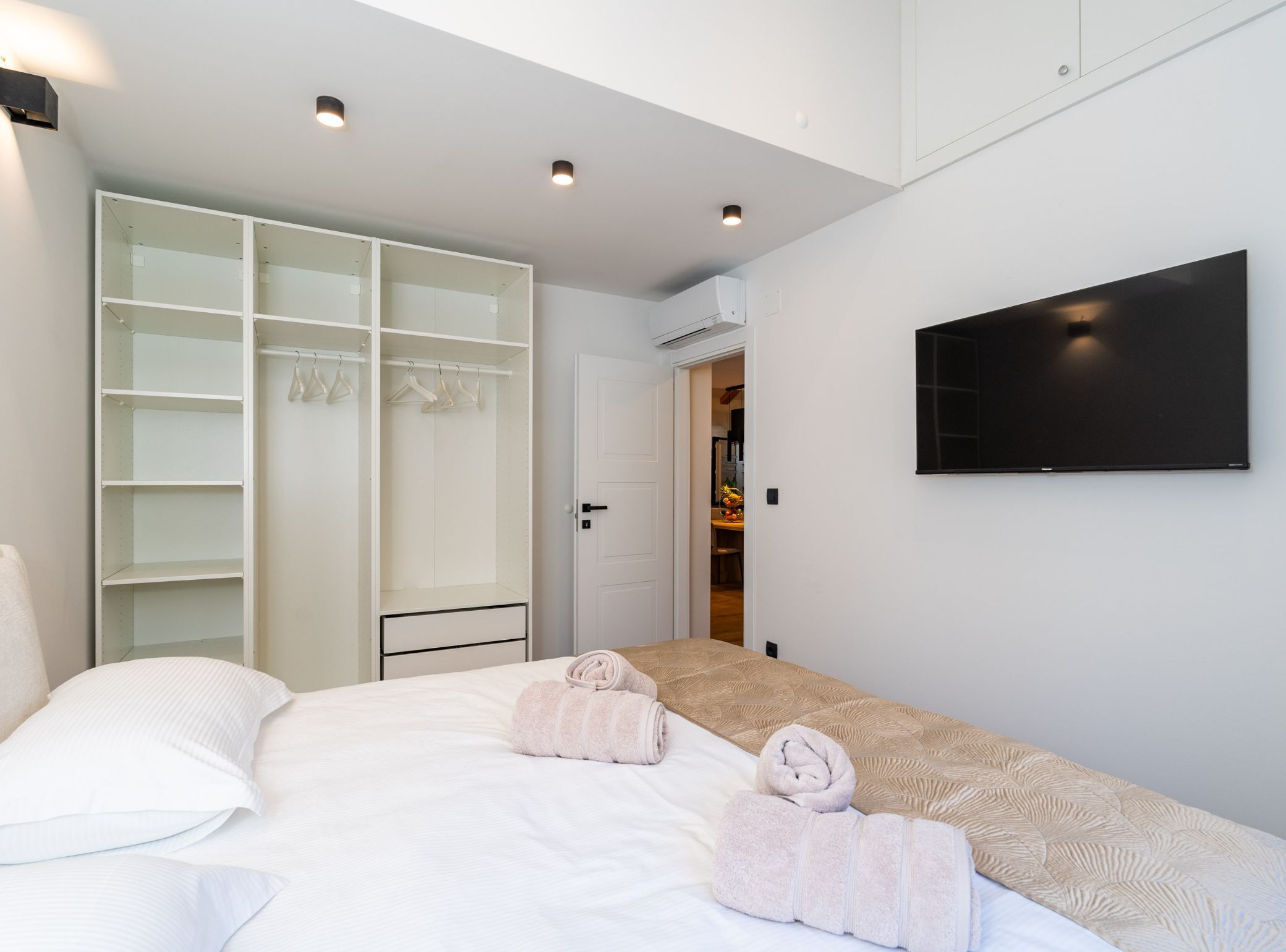 A modern bedroom with a bed, a walk-in closet, and a flat-screen TV on the wall.