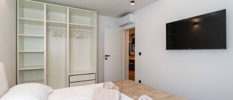 A modern bedroom with a bed, a walk-in closet, and a flat-screen TV on the wall.
