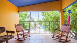 Un balcon avec deux fauteuils à bascule en bois, un sol carrelé et une vue sur la verdure.