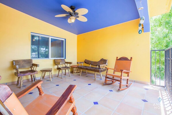 A room with a yellow and blue color scheme, wooden furniture, a ceiling fan, and a view of greenery outside.