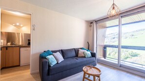 Ein modernes Wohnzimmer mit einem grauen Sofa, einem kleinen Holztisch und einem großen Fenster mit Blick auf die Landschaft.