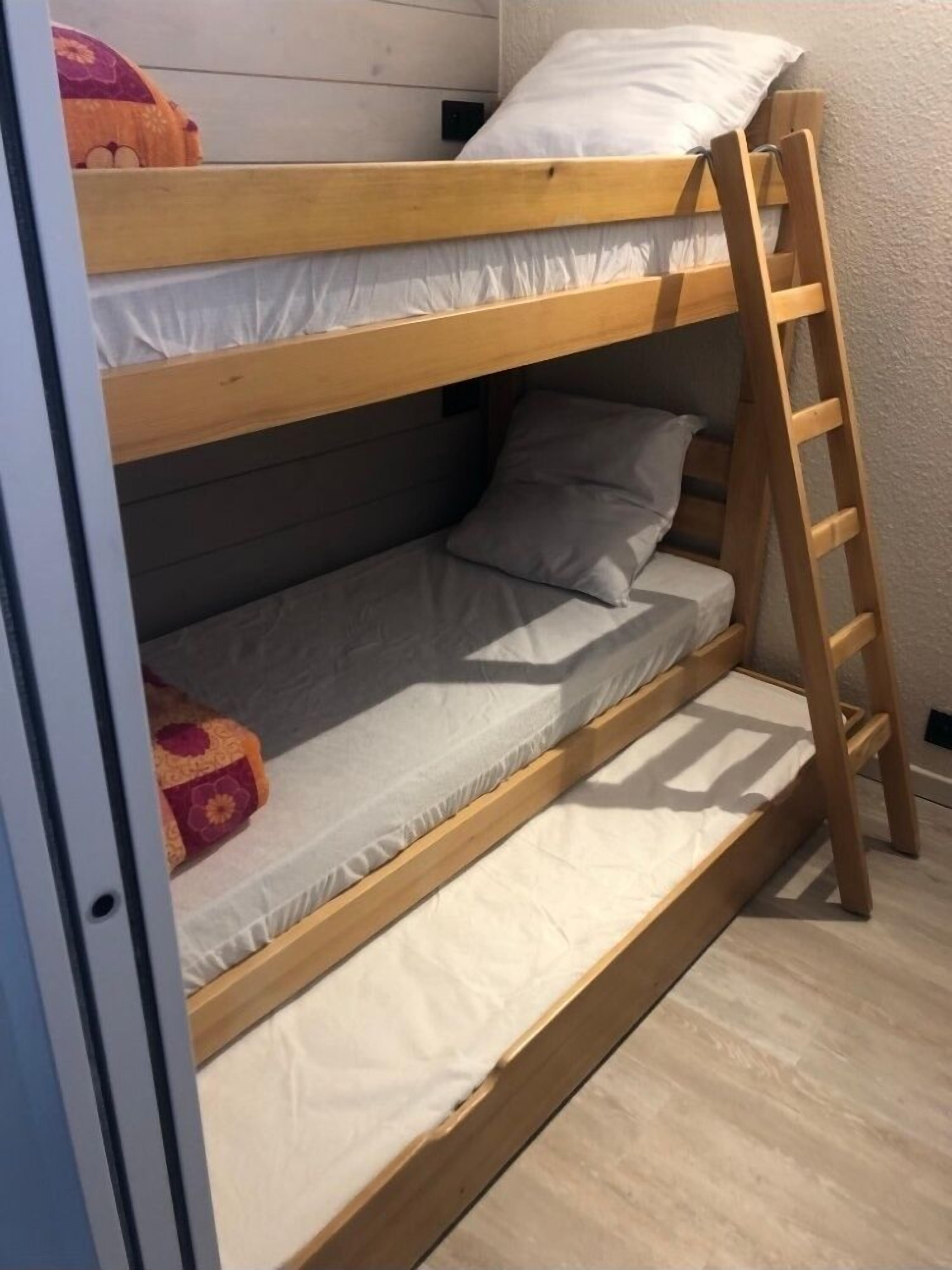 A bunk bed with a wooden ladder, a pillow, and a blanket.