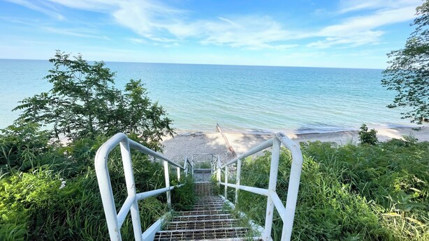 En trappe ned til en strand med kig til havet.