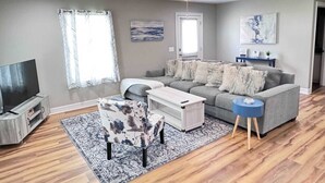 Una sala de estar con un sofá gris, una mesa de centro, un mueble para televisor y una alfombra estampada.