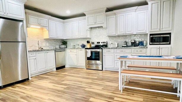 Una cocina moderna con armarios blancos, electrodomésticos de acero inoxidable y piso de madera.