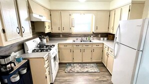 Une cuisine de taille réduite avec des meubles de couleur beige, un réfrigérateur blanc et une cuisinière à gaz.