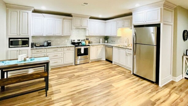 Une cuisine moderne avec des armoires blanches, des appareils en acier inoxydable et un plancher en bois.