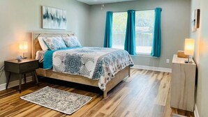 Une chambre à coucher comprenant un lit, des tables de chevet, un ventilateur de plafond, une fenêtre avec des rideaux et un tapis.