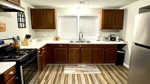 A kitchen with wooden cabinets, a stainless steel refrigerator, a gas stove, and a window with blinds. - Quiet & Cozy in 3BR 2BA (Port Neches)
