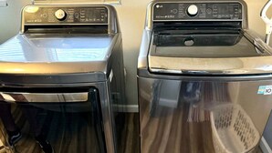 Two front-loading washers in a laundry room with a wooden floor and a window with blinds. - Quiet & Cozy in 3BR 2BA (Port Neches)