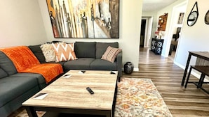 A modern living room with a sectional sofa, a coffee table, and a large abstract painting. - Quiet & Cozy in 3BR 2BA (Port Neches)