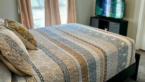 A neatly made bed with a patterned bedspread, a television on a stand, and curtains on the window. - Quiet & Cozy in 3BR 2BA (Port Neches)