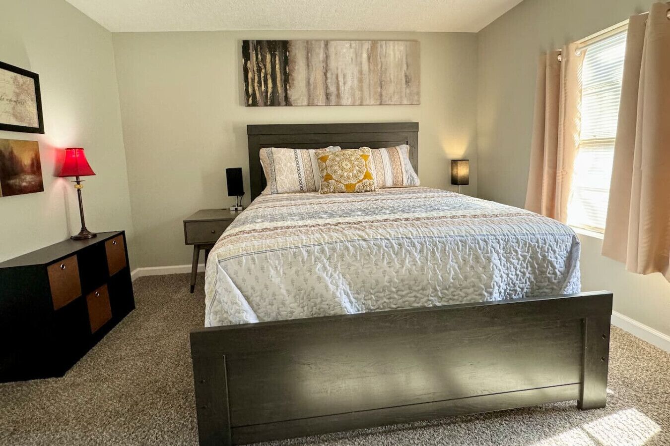 A bedroom with a large bed, a nightstand, a lamp, and a wall-mounted artwork.