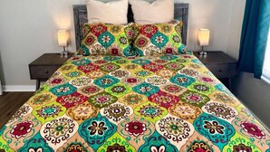 A bed with a colorful patterned bedspread, two pillows, and two bedside tables with lamps. - Bright & Airy 2BR 1BA Home Near The Riverfront (Port Neches)