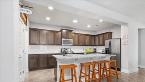 A modern kitchen with wooden cabinets, a central island with stools, a stainless steel refrigerator, and a microwave. - Perfect house for vacation or work w/Patio, Yard & Parking! 5 min from Kalahari! (Round Rock)