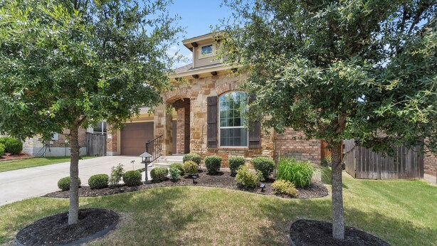 A two-story house with a stone facade, a large window, and a well-maintained lawn with trees and shrubs. - Perfect house for vacation or work w/Patio, Yard & Parking! 5 min from Kalahari! (Round Rock)