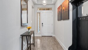 A hallway with a white door, a small table with a vase of flowers, and two paintings on the wall. - Perfect house for vacation or work w/Patio, Yard & Parking! 5 min from Kalahari! (Round Rock)
