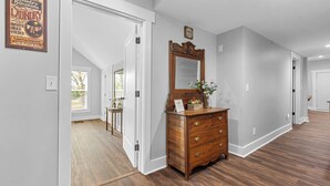 A hallway with a wooden dresser, a mirror, and a laundry service sign on the wall. - Farmhouse at Magnolia Valley (Fort Valley)