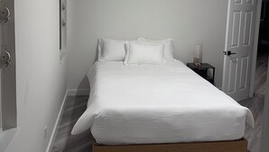A bedroom with a bed, a ceiling fan, a nightstand with a lamp, and a door.