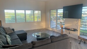 A modern living room with a sectional sofa, a glass coffee table, and a flat-screen TV mounted on the wall.
