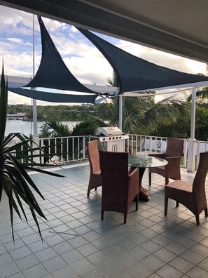 Un patio exterior con una parrilla, sillas de mimbre y vistas al agua.