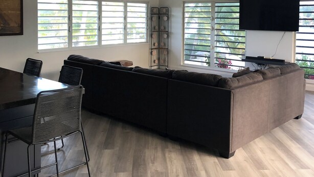 A modern living room with a sectional sofa, dining table with chairs, a ceiling fan, and a flat-screen TV.