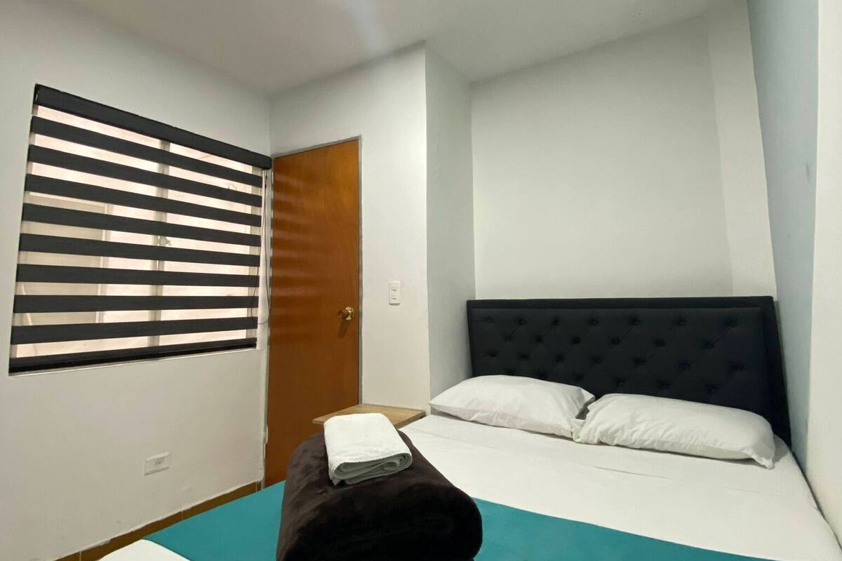 A hotel room with a bed, a window with blinds, a door, and a light fixture.