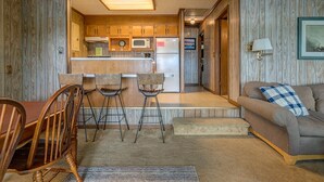 A cozy living room with a wooden floor, a brown sofa with a blue and white checkered pillow, and a dining area with a wooden table and two chairs. - Dewitt -Cozy cabin in the woods- perfect for a small family and a dog near SML State Park (Huddleston)