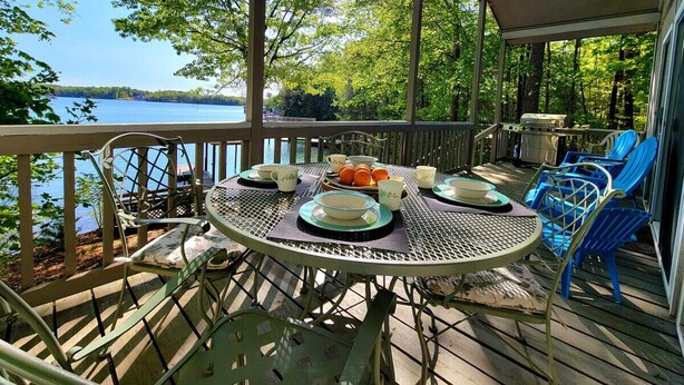 A covered outdoor deck with a table set for dining, surrounded by chairs, overlooking a lake. - Dewitt -Cozy cabin in the woods- perfect for a small family and a dog near SML State Park (Huddleston)