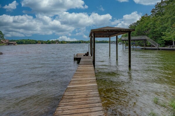 A wooden pier extending into a calm lake, with a covered seating area and a staircase leading to a dock.
