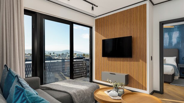 Una habitación de hotel moderna con un ventanal grande, un televisor de pantalla plana montado en un panel de madera, un sofá con una manta y una pequeña mesa redonda con un florero.