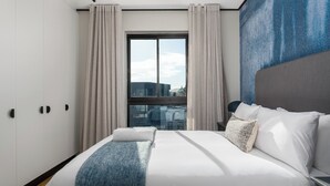 Un hotel moderno con una cama grande, vistas a edificios a través de una ventana y una pared de acento azul.