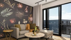 Ein modernes Wohnzimmer mit einem grauen Sofa, einem runden Couchtisch und einer Wandmalerei mit floralem Muster.